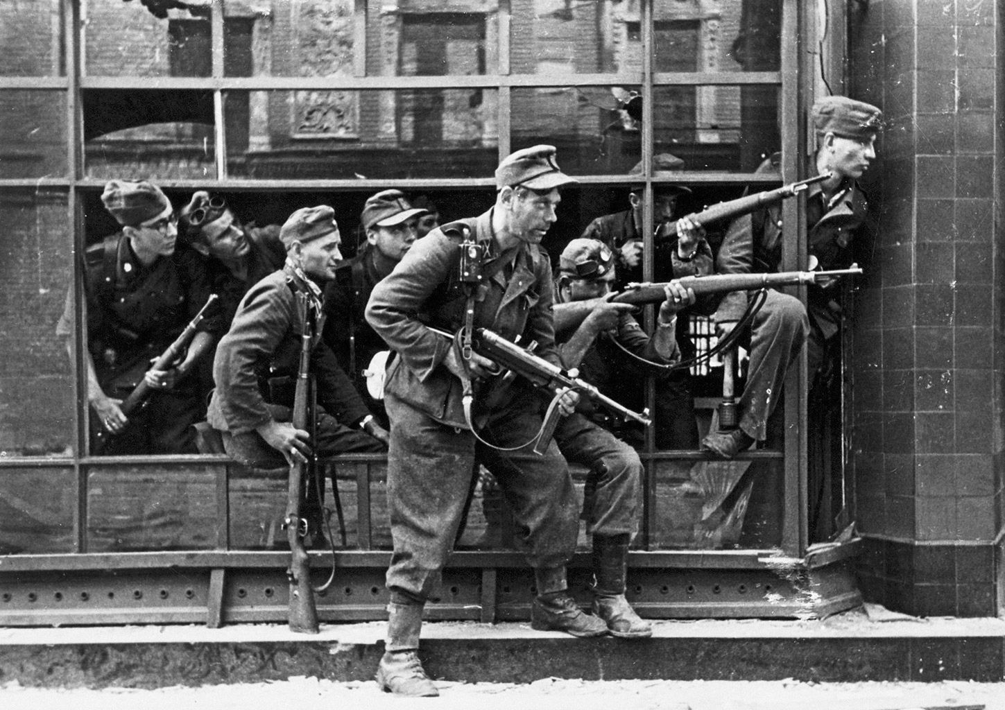 SS-Soldaten der Brigade Dirlewanger im Fenster eines Stadthauses in der Focha-Straße 9. In der Spiegelung des Glases sind Details des Stadthauses auf der gegenüberliegenden Straßenseite in der Focha-Straße 8 zu erkennen.